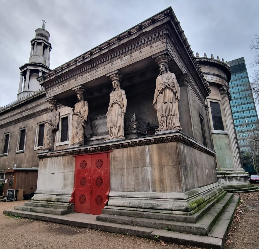 Facciata della Crypt Gallery di Londra con le sue caratteristiche cariatidi e la porta rossa centrale

